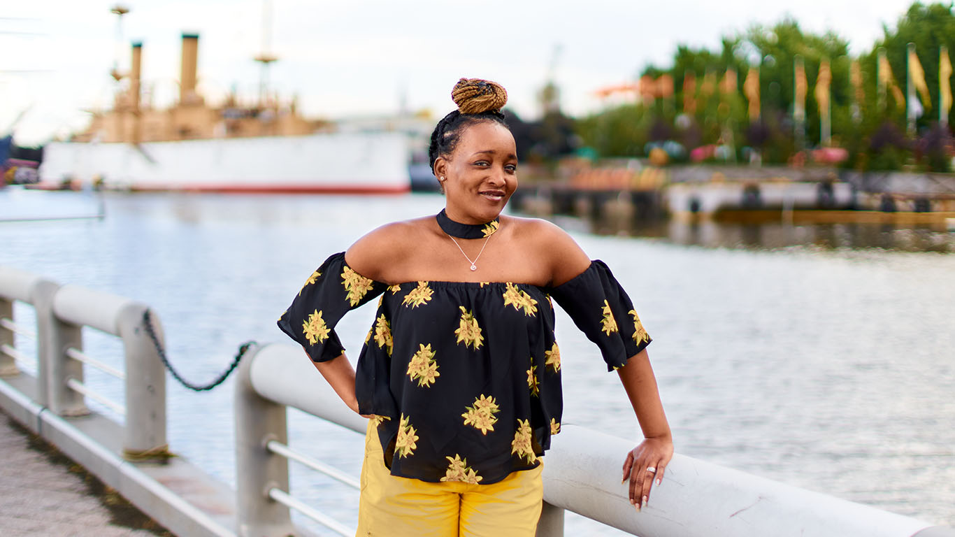 A woman with a top bun and tropical clothes smiles and dances in the camera