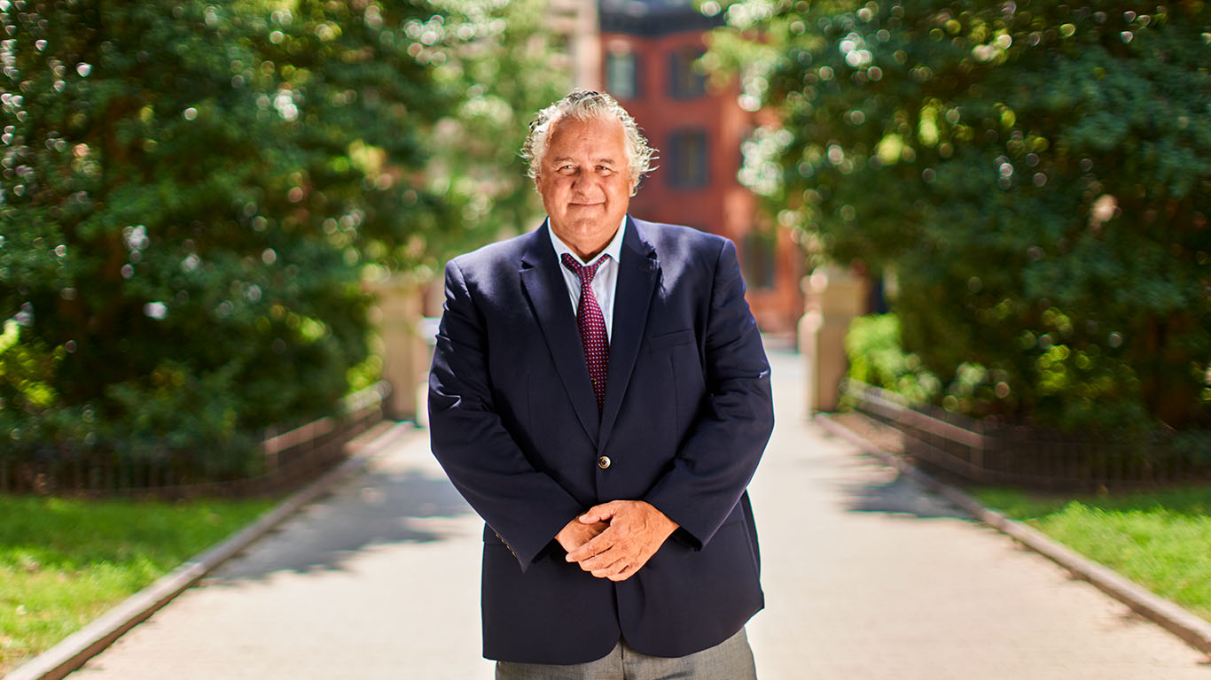 An older man in a suit holds his hands out and smiles